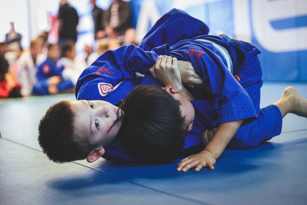 Two children in blue Gracie Barra uniforms practicing Brazilian Jiu-Jitsu on the mats
